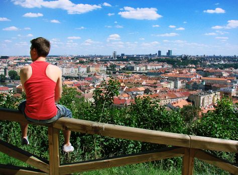 A guy sitting on a fence against panorama of the city