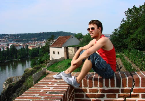 A guy sitting on a fence against panorama of the city