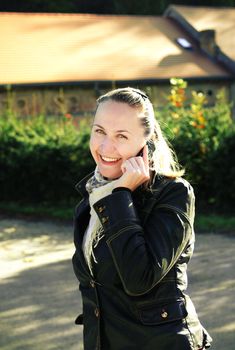 A smiling young woman talking on the mobile phone, outdoors background