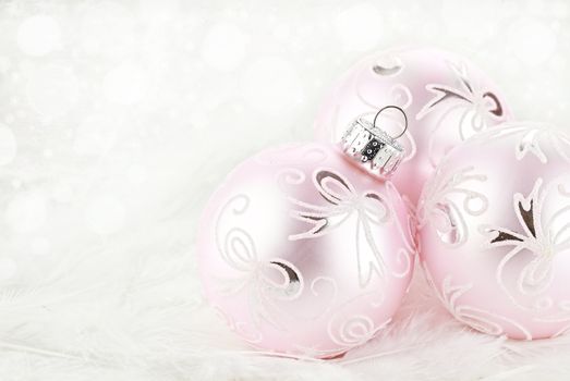 Macro of pink Christmas ornamets lying on a background of white feathers. Extreme shallow depth of field.