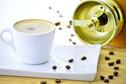white cup of coffee on a plate in front of a coffee grinder
