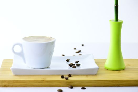 coffee beans and cup of coffee on a plate next to a bamboo on white backgraund