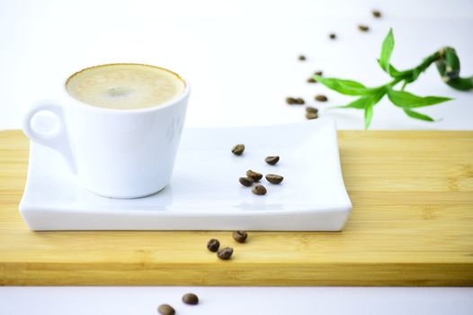 coffee beans and cup of coffee on a plate next to a bamboo on white backgraund