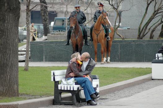 Moscow, Russia - April 2005. The man and the woman kiss on a bench. At a background two police officers on horses.