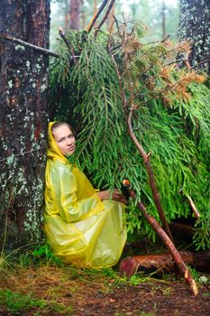 Young woman wearing yellow raincoat sitting in a shelter of branches