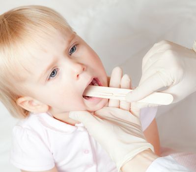 Pediatrician examining little girl's throat with tongue depressor