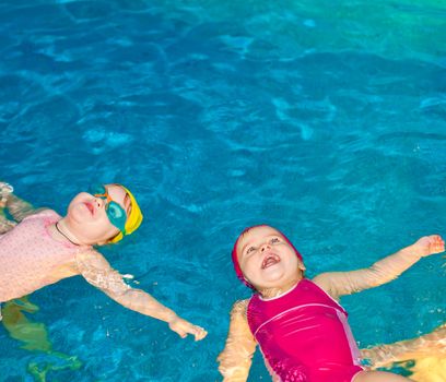 Two happy little girls learning to swim in a pool