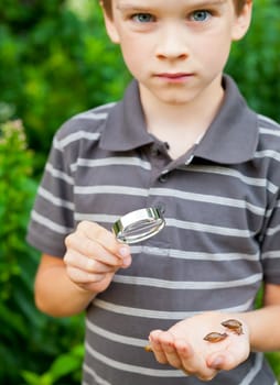 Young boy with loupe holding snails on his palm, focus on loupe