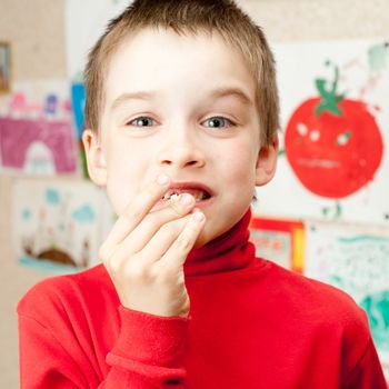 Boy shows lost deciduous teeth against his drawing on the wall