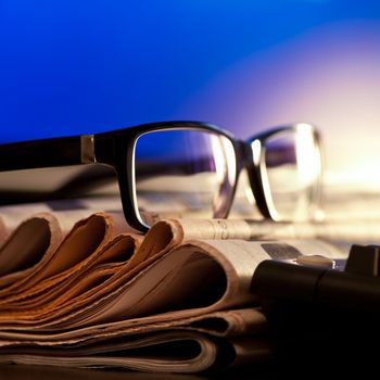 Glasses on stack of newspapers against blue screen