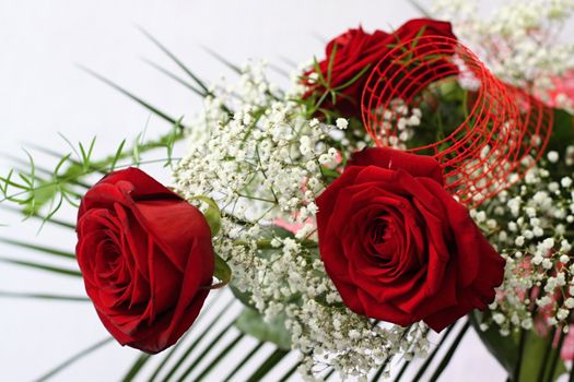 Three red roses and whitte flowers with green leafs