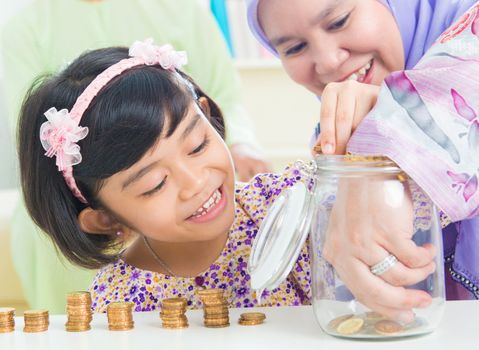 Muslim mother and daughter saving money at home. Southeast Asian family living lifestyle.