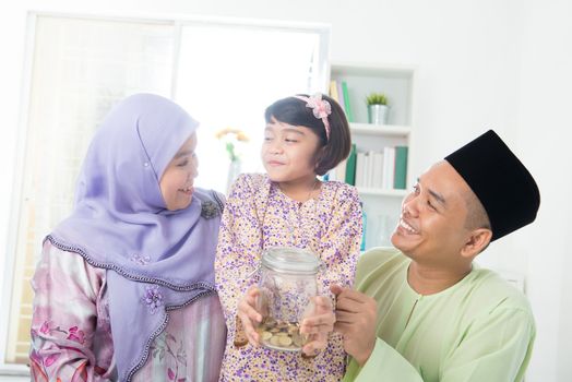 Southeast Asian family. Muslim girl hand holding money jar at home.