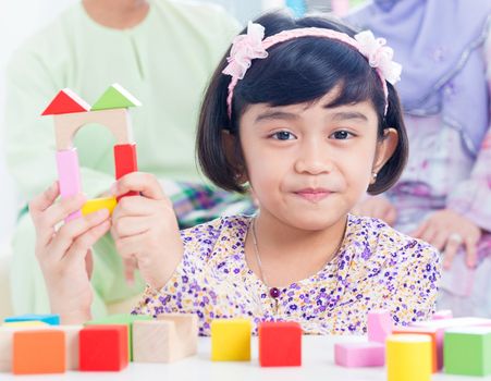 Muslim child building wooden house. Southeast Asian girl playing woodblock house at home.