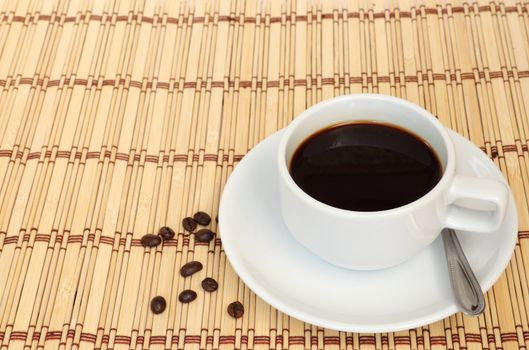 Cup of coffee with some coffee beans next to the cup, put on the table cloth made from wooden.