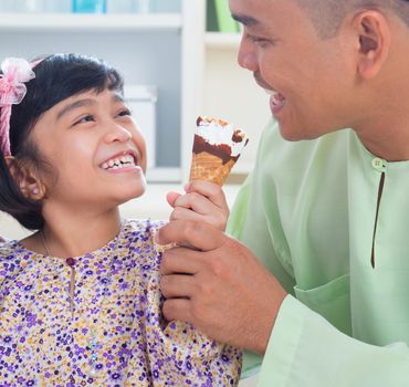 Cute Southeast Asian girl feeding ice cream to father. Malay Muslim family lifestyle