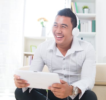 Asian man listen music with headphone, sitting on floor at home.