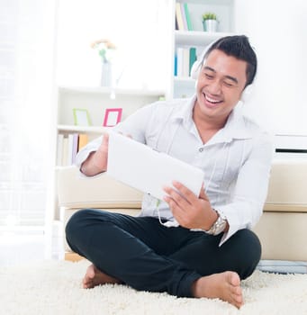 Asian man listen song with headphone, sitting on floor at home.