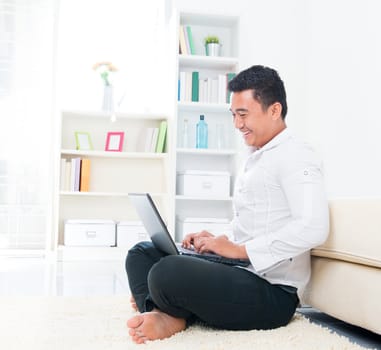 Asian man browsing internet at home, sitting on floor.