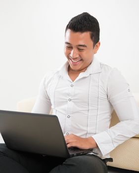 Southeast Asian man sitting on floor, browsing internet.