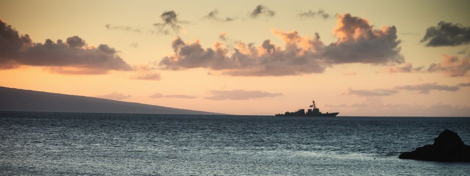 United States Navy ship underway off the coast of Maui, Hawaii. Dramatic clouds and the Island of Lanai in the background