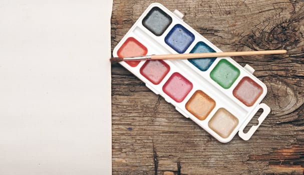 water-color, brush and palette with canvas on old wooden background