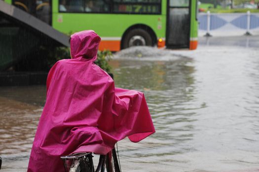 Girl stranded in flooding water, pushing her bike, in heavy rains