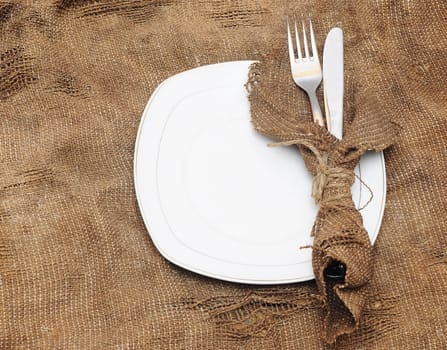 empty white plate fork and knife on brown sacking texture
