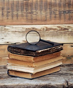 Stack of antique books with magnifying glass on wooden table