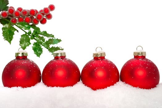 Close up of decorative Christmas ornaments on the snow, and holly.