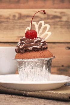 Cupcake with chocolate cream and cherry on old wooden background