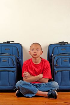 A boy sitting in front of suitcases appears upset.