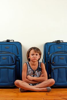 A young girl sits in front of suitcases, with a sad expression on her face.