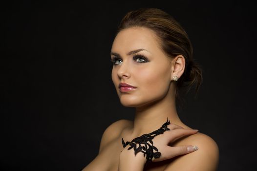 Beautiful pensive elegant woman with bare shoulders and a stylish lace glove staring up onto the air lost in thought, head and shoulders studio portrait on a dark background