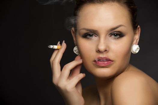 Cropped head and shoulders studio portrait of a stylish beautiful young woman smoking a cigarette copy space