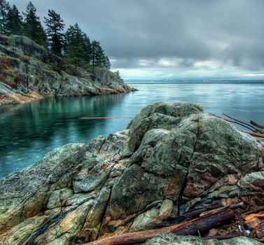 Cool tone photo along a rocky shore with the Vancouver city skyline in the distance.