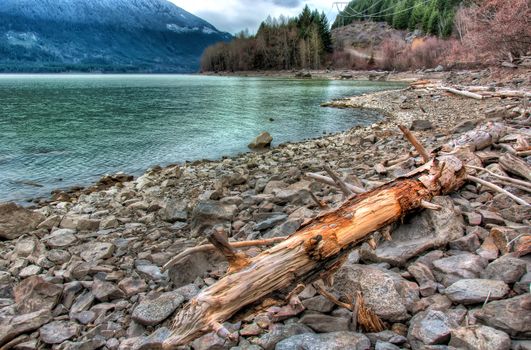 Log beside a turquoise lake on rocky shoreline