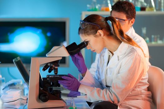 Attractive young scientist and her post doctoral supervisor looking at the microscope slide in the forensic laboratory.