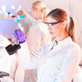 Attractive young researcher looking at the microscope slide in the forensic laboratory.