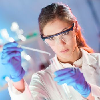 Focused young life science professional pipetting solution into the glass cuvette. Lens focus on the researcher's eye.