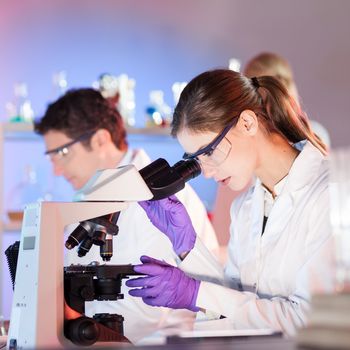 Attractive young researcher looking at the microscope slide in the life science laboratory.