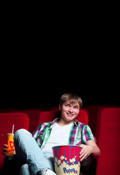 man in a movie theater, watching a movie and drink a drink