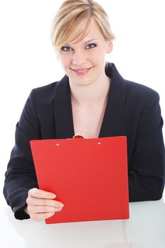 Cheerful businesswoman with a red clipboard sitting at a table smiling at the camera isolated on white