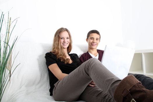 Low angle view of a smiling teenaged brother and sister relaxing together on a couch sharing a laptop as they surf the web