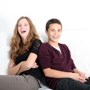 Laughing teenaged brother and sister sitting leaning on each other enjoying a good joke, square format with copyspace