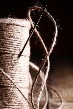 Artistic image of spool of thread and needle over wooden surface