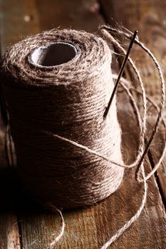 Artistic image of spool of thread and needle over wooden surface