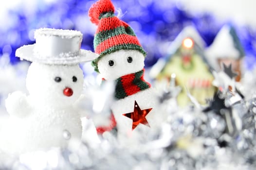 two snowmen in front of a house in artificial snow on white and blue background