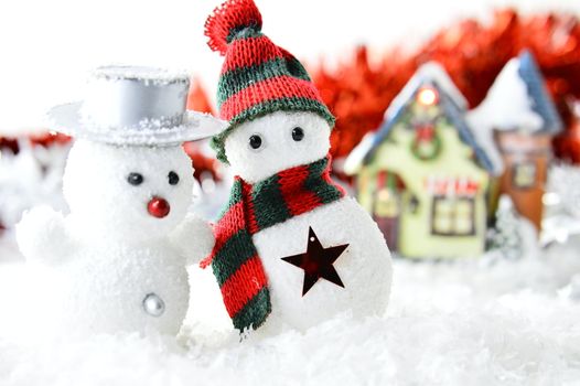 two snowmen in front of a house in artificial snow on white and red background