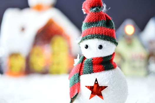 snowman with black and red hat and scarf in artificial snow on dark background